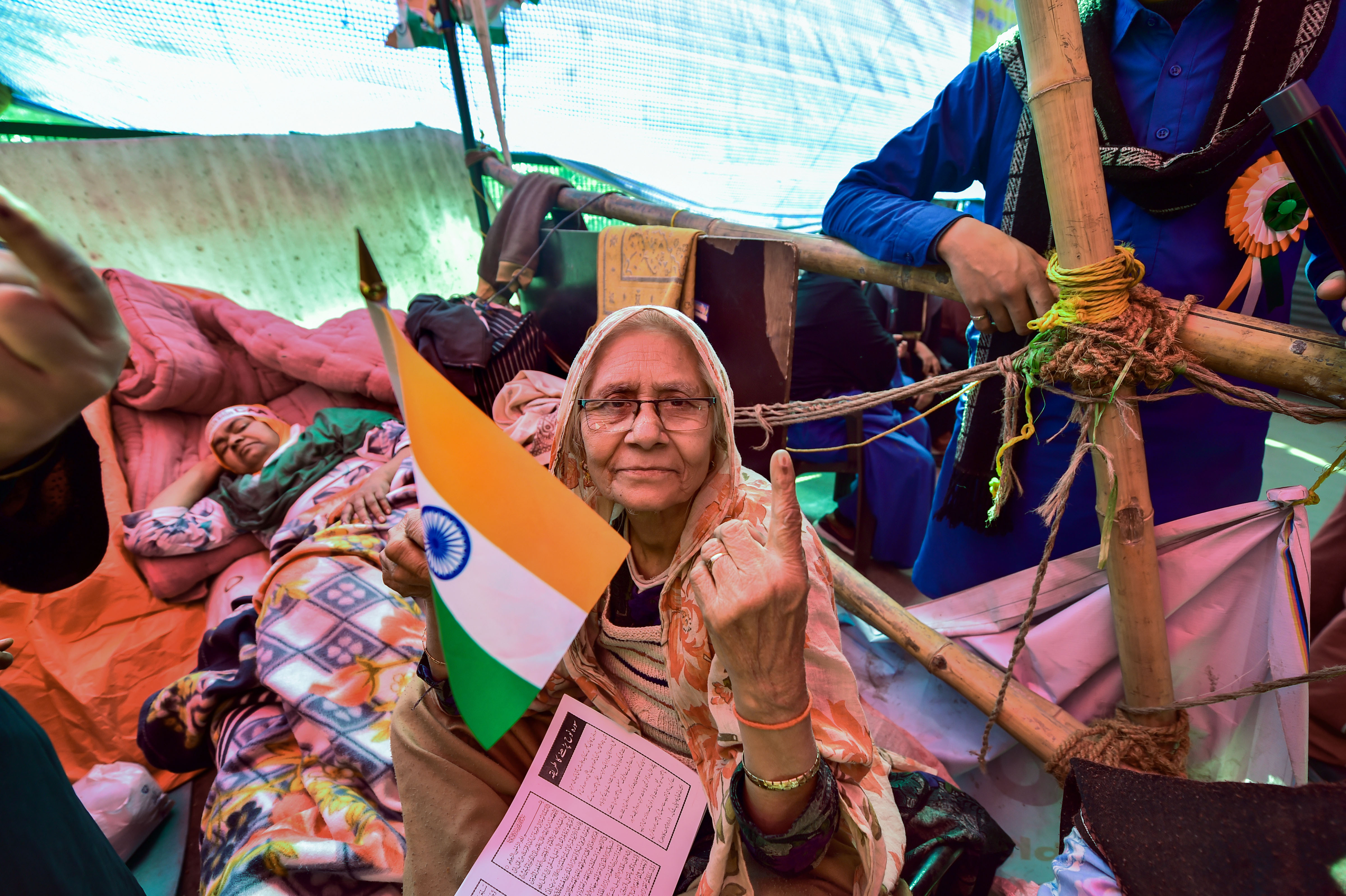 ؤنئی دہلی کے شاہین باغ میں ، ایک مظاہرین ، جس نے ترنگا پکڑا ہوا ہے، دہلی اسمبلی انتخابات میں ووٹ ڈالنے کے بعد اپنی انگلی پر سیاہی کا نشان دکھاتے ہوئے ۔ تصویر : پی ٹی آئی